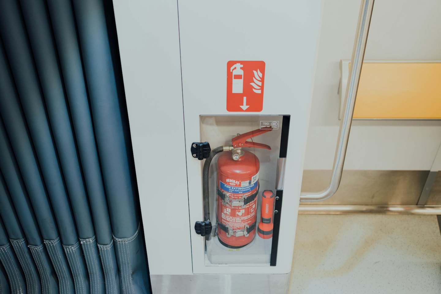 Red fire extinguisher mounted inside a white wall panel.