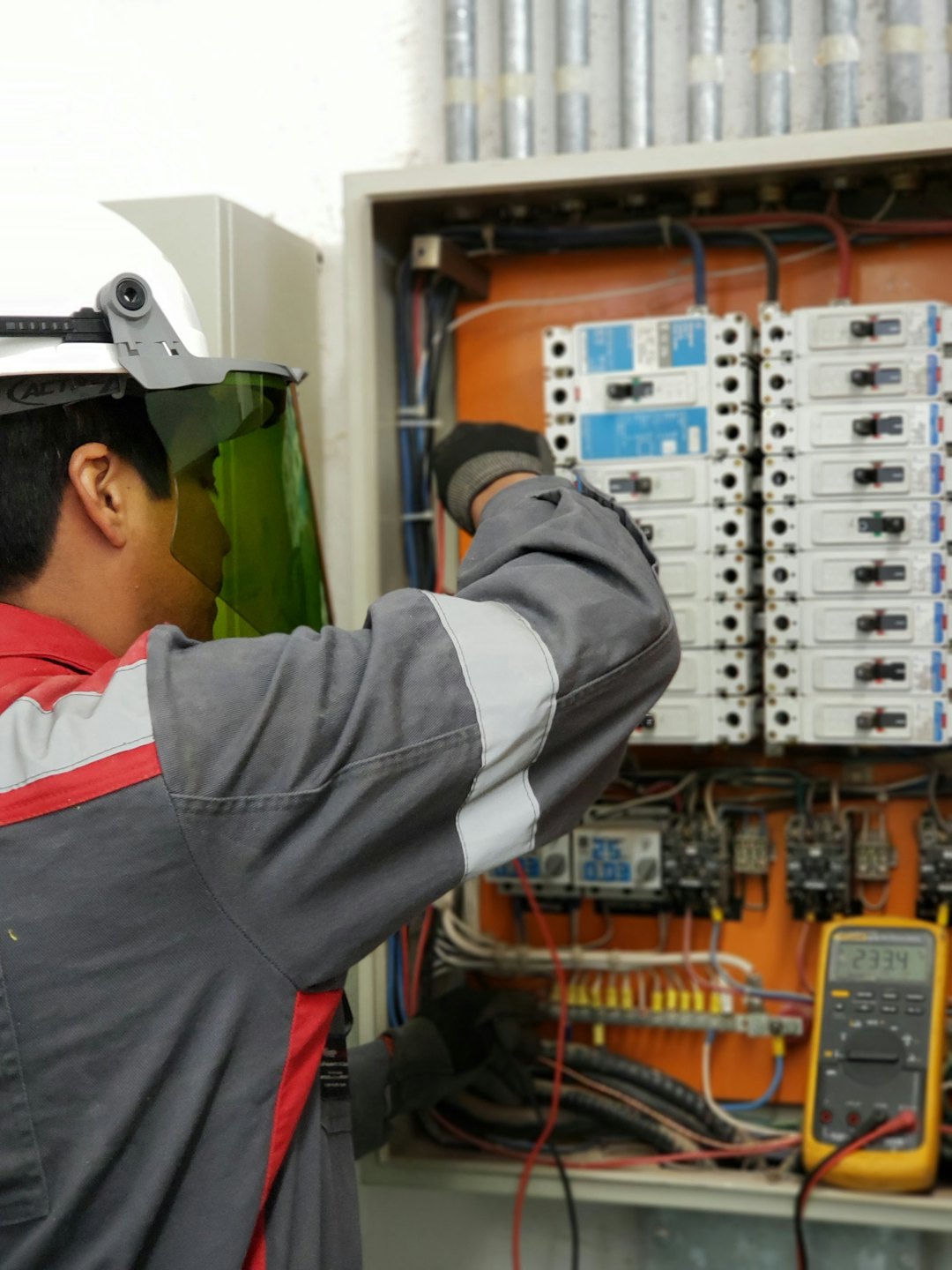 Technician inspects open electrical panel with circuit breakers and wiring.